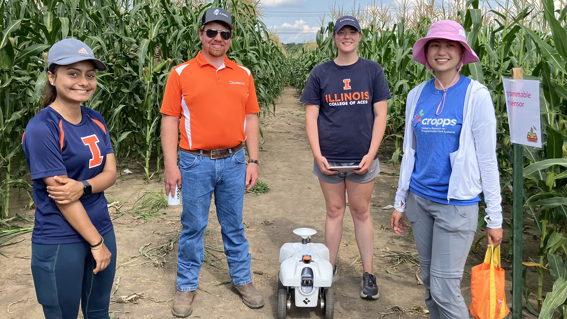 four people with a wheleled robot in a field of corn